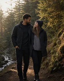A couple walks together on a forest trail beside a stream