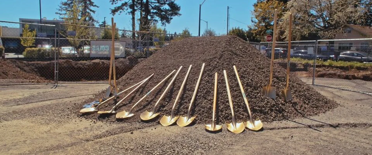 Ceremonial gold shovels line the ground before an outdoor groundbreaking event