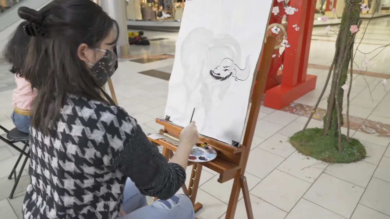 An artist paints on an easel during a Lunar New Year event at Washington Square Mall