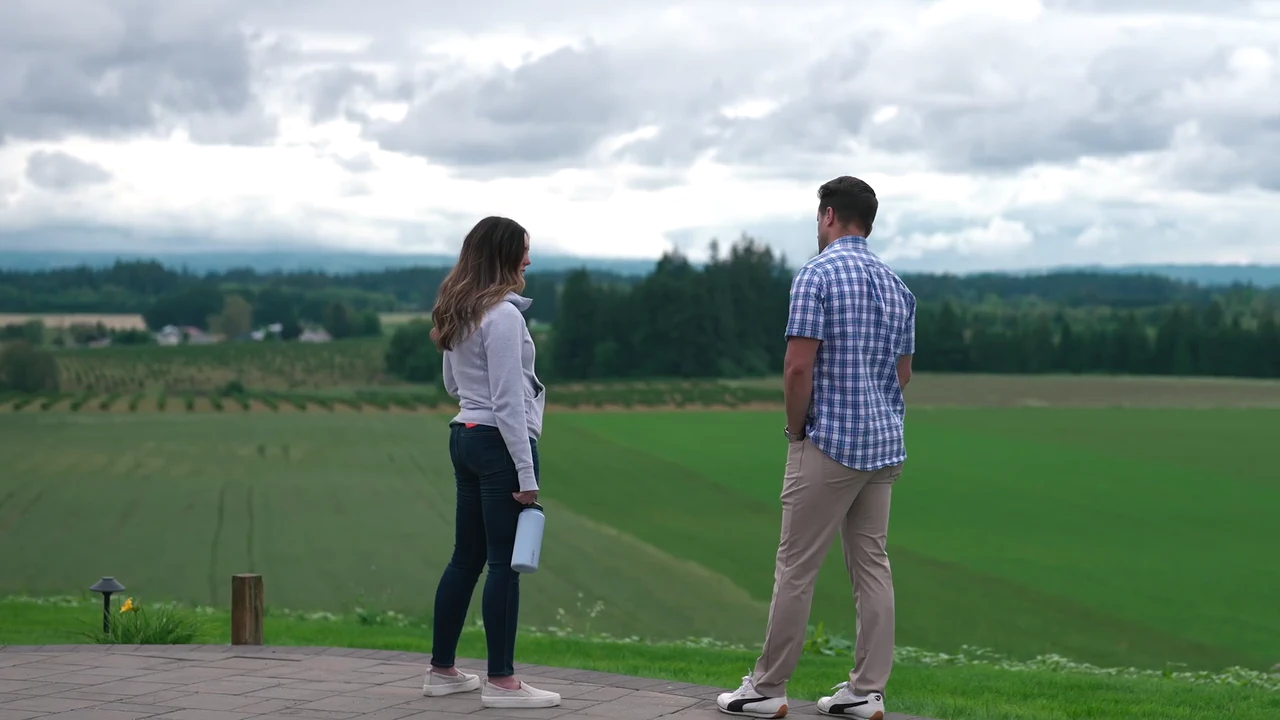 Two people talk on a hillside overlooking green fields
